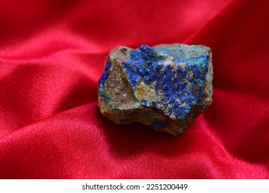 Isolated rough azurite on scarlet background, day light shot.A closeup of deep blue brown mineral on wrinkled fabric, geology, mineralogy, jewelry material.Primary colors, macro shot. - Shutterstock ID 2251200449