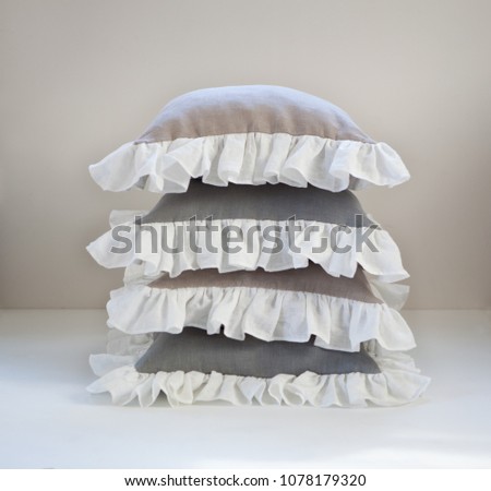 Isolated ruffled throw pillow stack for home decor. Gray and beige pillows with white ruffles.