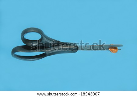 Isolated scissors is cutting a penny in half.  Blue background.