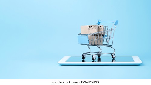 Isolated of Shipping paper boxes inside blue shopping cart trolley on tablet with blue background and copy space , Online shopping and e-commerce concept.