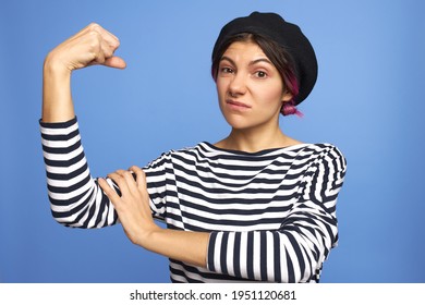 Isolated Shot Of Angry Strong Young Woman With Nose Ring Clenching Fist, Demonstrating Arm Muscle, Making Displeased Grimace, Can Stand For Herself. Strength, Energy, Self-defense And Confidence