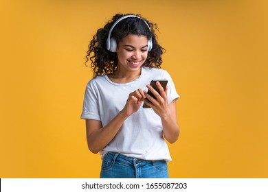 Isolated shot of beautiful casually dressed girl with cute perfect smile wearing  basic white t-shirt, jeans and wireless headphones enjoying her day-off listening to music browsing her smartphone.  - Shutterstock ID 1655087203