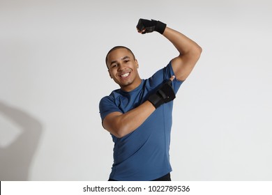Isolated shot of cheerful handsome young African male athlete in blue t-shirt smiling broadly, flexing muscles and pointing finger at his bicep. People, sports, activity and healthy lifestyle concept - Powered by Shutterstock