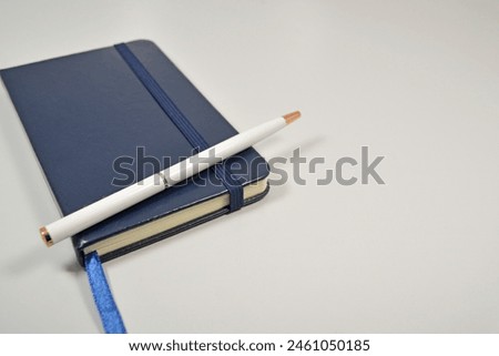 Isolated small blue notebook with a white pen placed on the left side of a white background with blank space on the right.