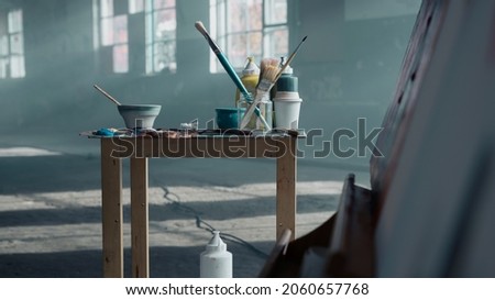 Isolated Small Table Standing in the Middle of an Empty Abandoned Warehouse With Artist Tools and Paint Equipment.