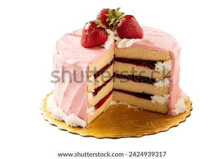 An isolated Strawberry Cream Cake topped with strawberries. Pink icing and strawberry fruit filling inside. Four layers with slice cut out to show. Sitting on a gold doily platter.