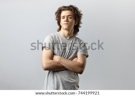 Isolated studio portrait of handsome self confident cool young American posing in studio with arms crossed and staring at camera with arrogant conceited look feeling proud of himself. Body language
