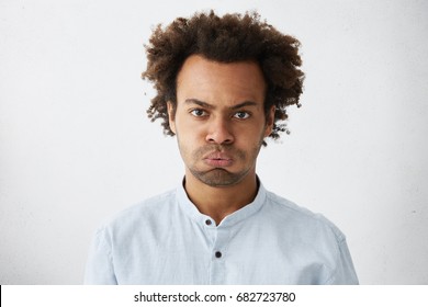 Isolated Studio Shot Of Unhappy Grumpy Serious Young African American Manager With Afro Hairstyle Frowning, Puffing His Cheeks, Feeling Fed Up As He Has To Stay At Office And Work Extra Hours.