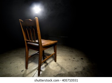 Isolated Wooden Chair In A Dark Scary Prison With An Interrogation Spotlight