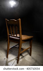 Isolated Wooden Chair In A Dark Scary Prison With An Interrogation Spotlight
