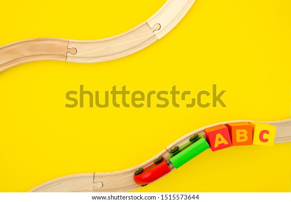 Isolated wooden train road on a yellow\
background with a toy a b c blocks. Construction of tracks with\
curves, the concept of Childhood\
minimalism