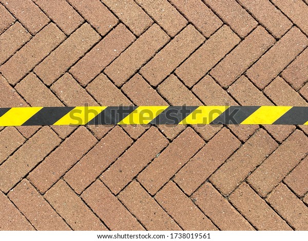 Isolated yellow black do not cross the border\
line tape on pavement divides a contigious connected surface into 2\
halves - New world order\
concept