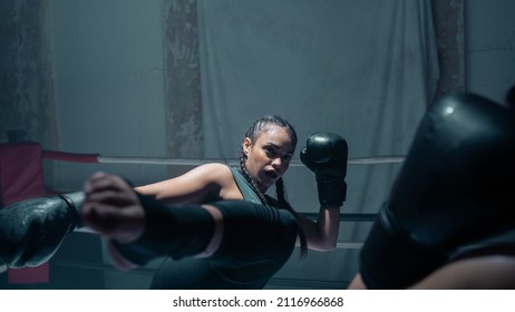 Isolated Young Ethnic Woman Doing a High Kick, Wearing Foot Pads and Black Boxing Gloves As She Trains In the Boxing Ring With Her Coach. Strong and Confident Female Athlete Showing Her Skills. - Powered by Shutterstock