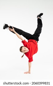 Isolated young Russian girl in red t-shirt hip hop break dancer dancing in studio in white background, performing freeze hand stand of downrock breakdance looking into the camera