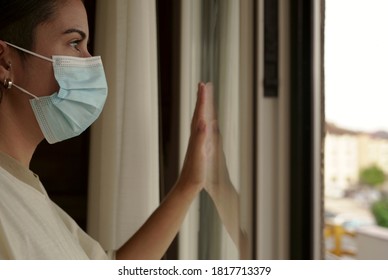 Isolated young woman at home by coronavirus looking out the window with her hand on the glass - Shutterstock ID 1817713379