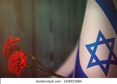 Israel flag with two red carnation flowers for honour of veterans or memorial day on light blue blurred natural wood wall mockup. Israel glory to the heroes of war concept.