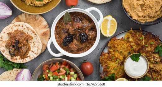 Israeli cuisine: esik fleisch - beef stew with damson plums and spices, hummus,  potato latkes, ptitim, a type of pasta also known as "Israeli couscous", pita bread, israeli salad. Grey background.