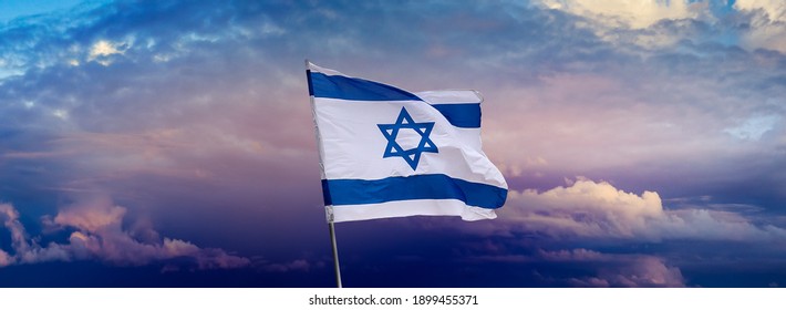 Israeli flag with a star of David over Jerusalem at cloudy sky background on sunset, panoramic view. Patriotic concept about Israel with national state symbols and copy space for wide banner. - Shutterstock ID 1899455371