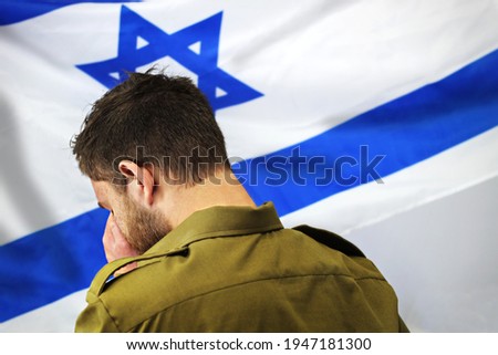 Israeli soldier crying in front of the flag of Israel