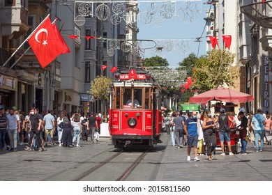 Istanbul, 28 july 2021, public tramway, nostalgic red retro tram on famous Istiklal Street Avenue, pedestriants, turkish flags, daily life Beyoglu distirict on europe side of city
