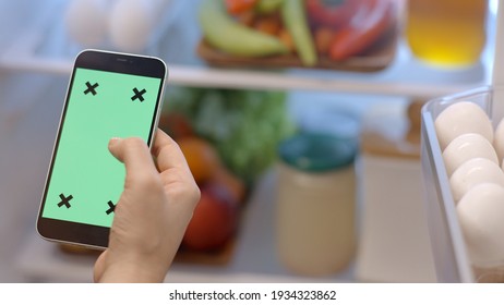 Istanbul, Turkey- 01.25.2021:Mobile phone with green screen tracking point with a refrigerator with vegetables and fruits in the background. On the phone, the woman scrolls and touches the screen.