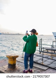 Istanbul, Turkey - 06.21.2022: Young Tourist Woman Taking Photograph Of Beautiful Sea View With Her Mobile Phone. Back View. She Has Cap On Her Head.