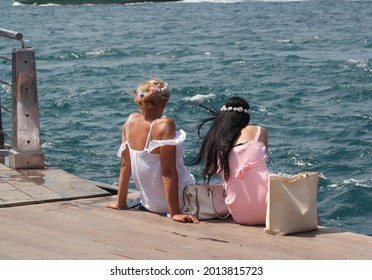istanbul Turkey, July 25, 2021, two women sitting near the sea and enjoying sunny windy summer day, have flower crown on their heads, blonde and black hairs