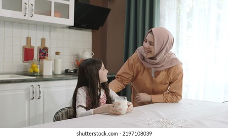 Istanbul,Turkey - 04.22.2022:She Gives Milk To Her Mother, Who Is Dressed In Hijab, To Drink. A Healthy Diet Is Important For A Child. The Girl Is Drinking Yogurt In The Kitchen And Licking Her Lips.