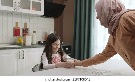 Istanbul,Turkey - 04.22.2022:She Gives Milk To Her Mother, Who Is Dressed In Hijab, To Drink. A Healthy Diet Is Important For A Child. The Girl Is Drinking Yogurt In The Kitchen And Licking Her Lips.