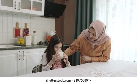 Istanbul,Turkey - 04.22.2022:She Gives Milk To Her Mother, Who Is Dressed In Hijab, To Drink. A Healthy Diet Is Important For A Child. The Girl Is Drinking Yogurt In The Kitchen And Licking Her Lips.