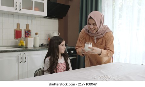 Istanbul,Turkey - 04.22.2022:She Gives Milk To Her Mother, Who Is Dressed In Hijab, To Drink. A Healthy Diet Is Important For A Child. The Girl Is Drinking Yogurt In The Kitchen And Licking Her Lips.