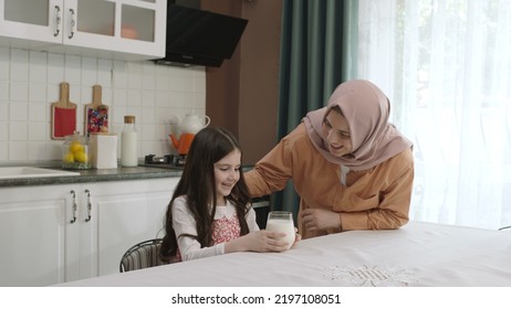 Istanbul,Turkey - 04.22.2022:She Gives Milk To Her Mother, Who Is Dressed In Hijab, To Drink. A Healthy Diet Is Important For A Child. The Girl Is Drinking Yogurt In The Kitchen And Licking Her Lips.