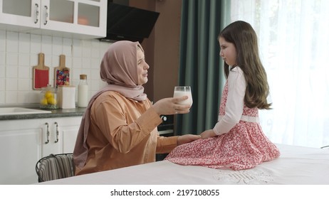 Istanbul,Turkey - 04.22.2022:She Gives Milk To Her Mother, Who Is Dressed In Hijab, To Drink. A Healthy Diet Is Important For A Child. The Girl Is Drinking Yogurt In The Kitchen And Licking Her Lips.