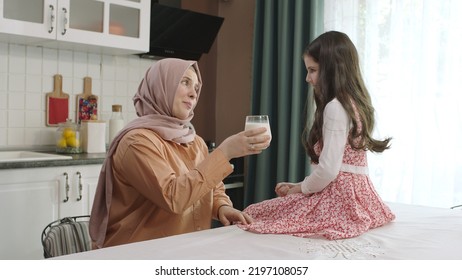 Istanbul,Turkey - 04.22.2022:She Gives Milk To Her Mother, Who Is Dressed In Hijab, To Drink. A Healthy Diet Is Important For A Child. The Girl Is Drinking Yogurt In The Kitchen And Licking Her Lips.