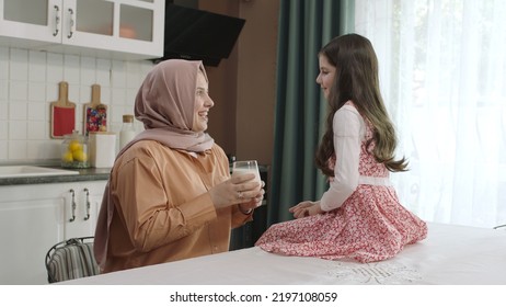 Istanbul,Turkey - 04.22.2022:She Gives Milk To Her Mother, Who Is Dressed In Hijab, To Drink. A Healthy Diet Is Important For A Child. The Girl Is Drinking Yogurt In The Kitchen And Licking Her Lips.