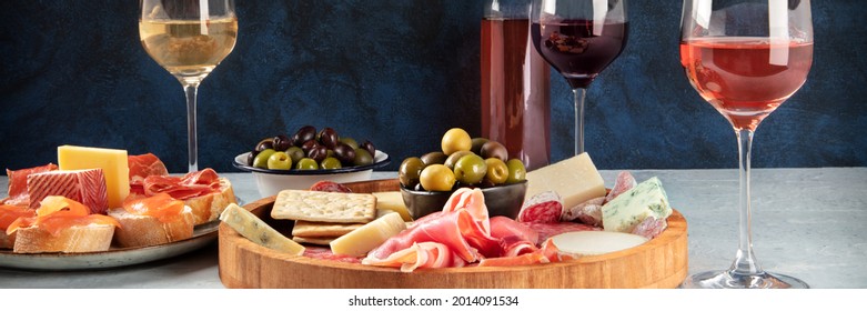 Italian antipasti or Spanish tapas panorama with wine, cold meat and cheese. Rose, white and red wine, a gourmet charcuterie and cheese platter and crostini with parma and salmon - Powered by Shutterstock