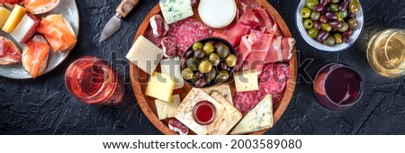 Italian antipasti or Spanish tapas panorama. Gourmet cold meat and cheese platter on a table, shot from the top with wine on a black background. A variety of appetizers