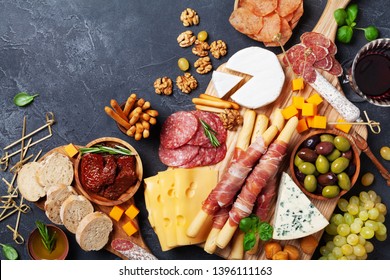 Italian appetizers or antipasto set with gourmet food on kitchen table top view. Mixed delicatessen of cheese and meat snacks with red wine.