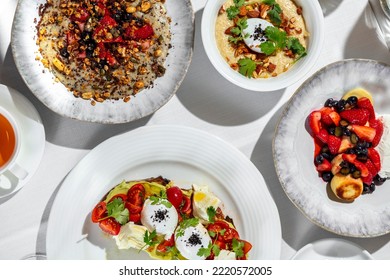Italian breakfast. There are four morning meals on a table with a white tablecloth. Cheesecakes with berries, oatmeal with berries, oatmeal with nuts and poached egg, bruschetta with avocado, tomato a - Shutterstock ID 2220572005