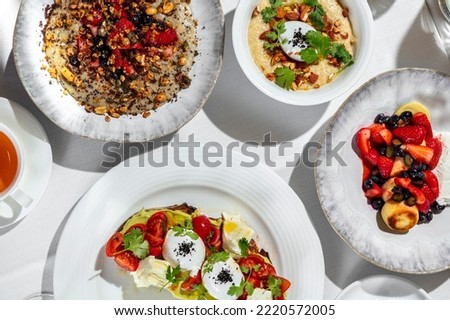 Italian breakfast. There are four morning meals on a table with a white tablecloth. Cheesecakes with berries, oatmeal with berries, oatmeal with nuts and poached egg, bruschetta with avocado, tomato a