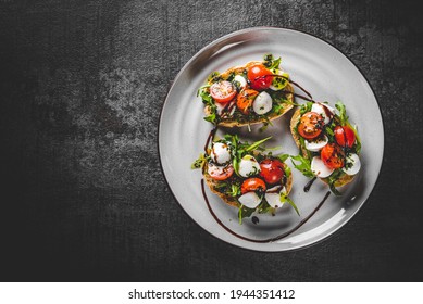Italian bruschetta with roasted tomatoes, mozzarella cheese, balsamic vinegar and herbs on plate on Dark grey black slate background