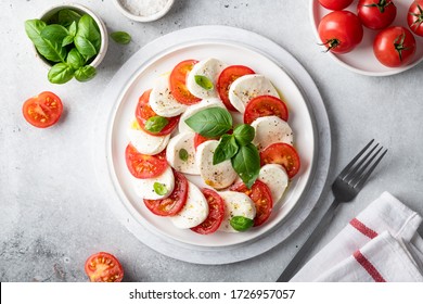 Italian caprese salad with sliced tomatoes, mozzarella, basil, olive oil on a light background. Top view. - Powered by Shutterstock