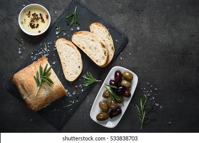 Italian Ciabatta Bread  On Black Slate Board With Herbs And Olives, Top View