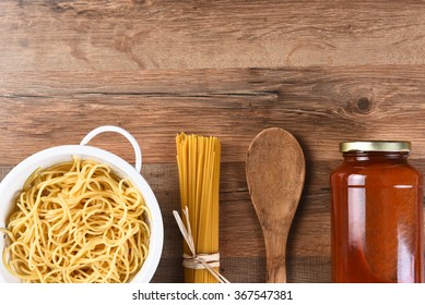 Italian Cooking Still Life With Copy Space. Wooden Spoon, Dry Spaghetti, Cooked Pasta And A Jar Of Sauce On A Wood Kitchen Table.