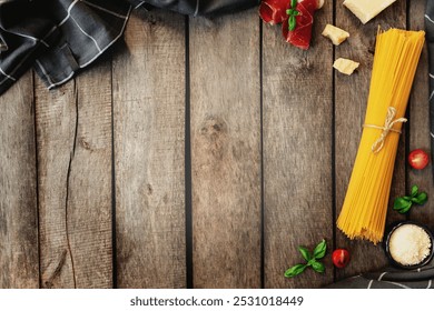 Italian cuisine concept flat lay. Parmesan Cheese chunks, grated cheese in black bowl, raw pasta, thinly sliced ham, cuts of cherry tomatos, basil leaves branches, kitchen towel on wooden background - Powered by Shutterstock