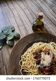 Italian delicious spaghetti carbonara pasta with bacon parmesan cheese garlic creamy sauce lies in a dark wooden round plate, bottle of olive oil, spices and a sprig of green leaves, top, close-up,