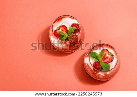 Italian dessert panna cotta in glass with strawberries. Healthy sweet food, trendy hard light, dark shadow. Light pink background, top view