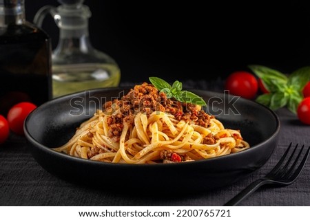 Italian dinner with Spaghetti or linguine with meat and tomato sauce bolognese on a black plate and dark background. Copy space.