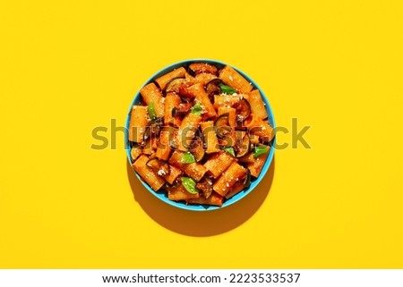 Italian dish, pasta with deep-fried eggplant, top view on a yellow-colored table. Pasta Alla Norma plate minimalist on a colorful background in bright light