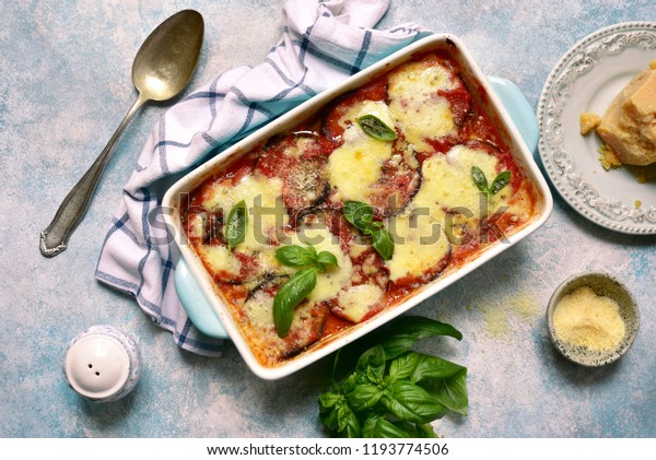 Italian eggplant dish melanzane alla parmigiana on\
a light blue slate, stone or concrete background.Top view with copy\
space.